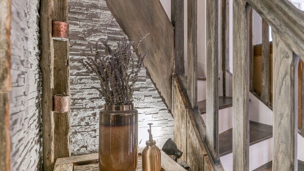 A rustic staircase with a wooden handrail, a stone wall, and a wooden table with a copper container and a bottle. - Vacation Home "Jacuzzi-Sauna Station 7 Laux" with Private Terrace, Shared Garden & Wi-Fi (Theys)