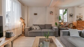 A modern living room with a grey sofa, a wooden coffee table, a TV, and a plant. - Vacation Home "Jacuzzi-Sauna Station 7 Laux" with Private Terrace, Shared Garden & Wi-Fi (Theys)
