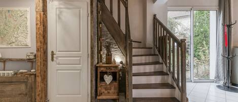 A staircase with wooden steps and a metal railing, a white door with a rustic wooden post, and a view of greenery outside.