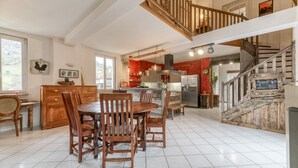A spacious kitchen with a dining area, wooden chairs, a central island, and a staircase leading to an upper level. - Vacation Home "Jacuzzi-Sauna Station 7 Laux" with Private Terrace, Shared Garden & Wi-Fi (Theys)