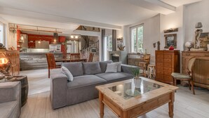A spacious living area with a gray sofa, wooden coffee table, and a dining area with chairs and a table. - Vacation Home "Jacuzzi-Sauna Station 7 Laux" with Private Terrace, Shared Garden & Wi-Fi (Theys)