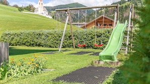 A playground with a slide, swings, and a building in the background.