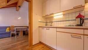 A kitchen with white cabinets, a wooden ceiling, a dining table with chairs, and a blue sofa in the adjacent living area.