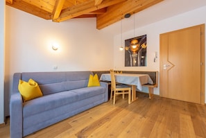 A room with a sofa, a dining table, a chair, a wooden door, and a ceiling with wooden beams.