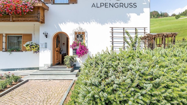 A building with a wooden balcony, a sign reading 'ALPENGRUSS,' and a stone pathway leading to the entrance.