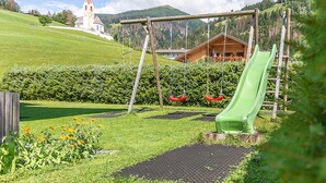 A playground with a slide, swings, and a building in the background. - Apartment 'Alpengruss Natura' with Mountain View, Shared Garden and Wi-Fi (Prato alla Drava)