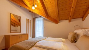 A bedroom with a wooden ceiling, a bed with white bedding, a bedside table, a mirror, and a window with curtains. - Apartment 'Alpengruss Natura' with Mountain View, Shared Garden and Wi-Fi (Prato alla Drava)