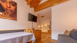 A compact living space with a dining table, a sofa, a TV mounted on the wall, and a kitchenette. - Apartment 'Alpengruss Natura' with Mountain View, Shared Garden and Wi-Fi (Prato alla Drava)