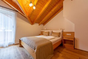 Une chambre à coucher avec un plafond en bois, un lit, une table de chevet et une fenêtre ornée de rideaux légers.