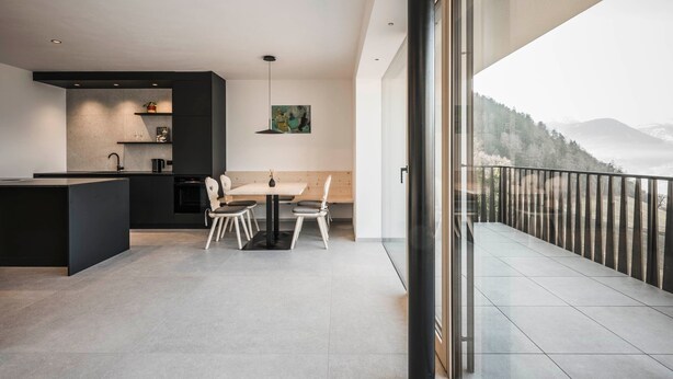 Una cocina moderna con comedor, un ventanal con vistas a montañas y un balcón con barandilla.