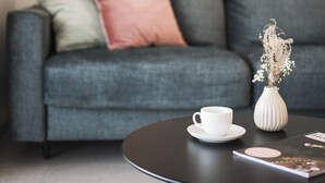 Una sala moderna con un sofá gris, una taza blanca sobre una mesa redonda y un jarrón con flores secas.