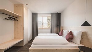 Un dormitorio con una cama de madera, un banco, un armario y una ventana con cortinas.