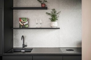 A modern kitchen with a black sink, two wine glasses, a potted plant, and a book on a shelf.