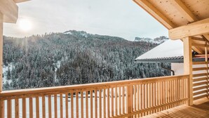 Ein Holzbalkon mit Blick auf einen verschneiten Wald und Berge.