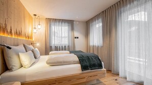 Una camera da letto con un letto, una testiera con un sistema di illuminazione, una finestra con tende leggere e una parete con pannello luminoso verticale.