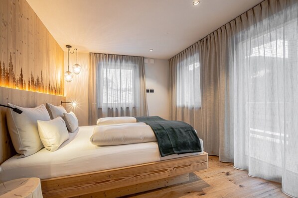Une chambre à coucher comprenant un lit, une tête de lit avec un luminaire intégré, une fenêtre avec des rideaux légers et un mur orné d’un panneau lumineux vertical.