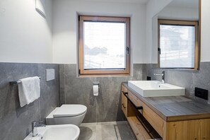 Une salle de bain moderne avec une grande fenêtre, des toilettes blanches, un lavabo et un meuble-lavabo en bois.