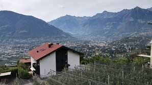A mountain view with a small building, a town below, and a valley. - Studio Apartment 'Spiess' with Mountain View, Shared Pool and Wi-Fi (Merano)