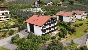 A modern two-story building with a red-tiled roof, surrounded by lush greenery and a well-maintained garden. - Studio Apartment 'Spiess' with Mountain View, Shared Pool and Wi-Fi (Merano)
