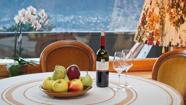 A dining table with a bowl of fruit, a bottle of wine, and two glasses. - Studio Apartment 'Spiess' with Mountain View, Shared Pool and Wi-Fi (Merano)