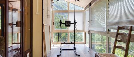 Una habitación con piso de madera, una silla de madera, una ventana con persianas y una puerta con panel de vidrio.