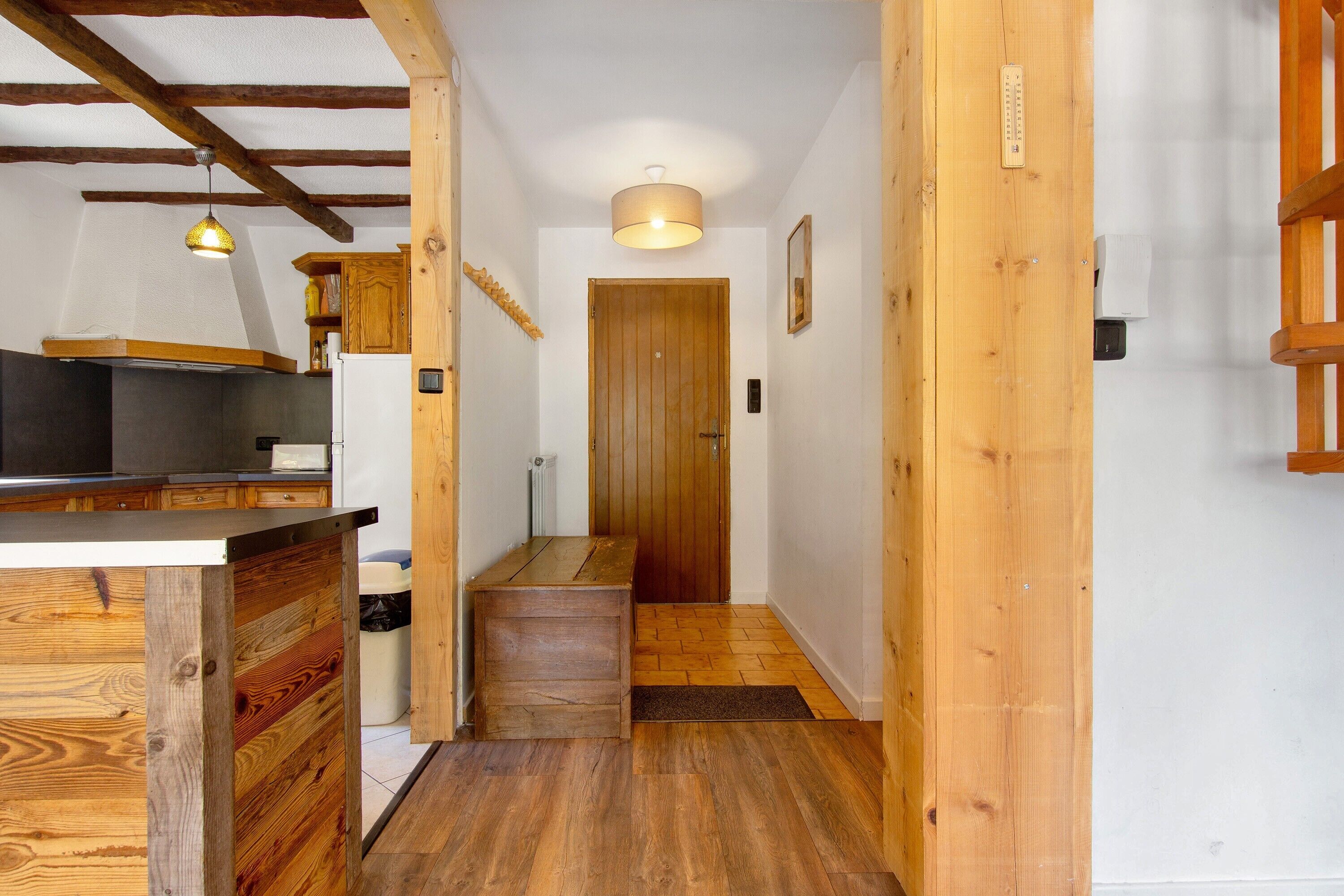 Un couloir intérieur en bois, avec un coin cuisine sur la gauche, une porte en bois au fond et un luminaire au plafond.