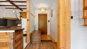 Un couloir intérieur en bois, avec un coin cuisine sur la gauche, une porte en bois au fond et un luminaire au plafond.