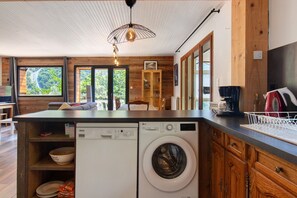 Een compacte keuken met een ingebouwde wasmachine en droger, houten kastjes en grote ramen met uitzicht op de omgeving.