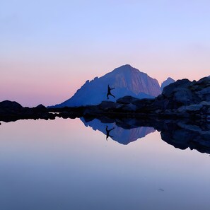 A mountain reflected in a calm body of water with a person jumping in the foreground.