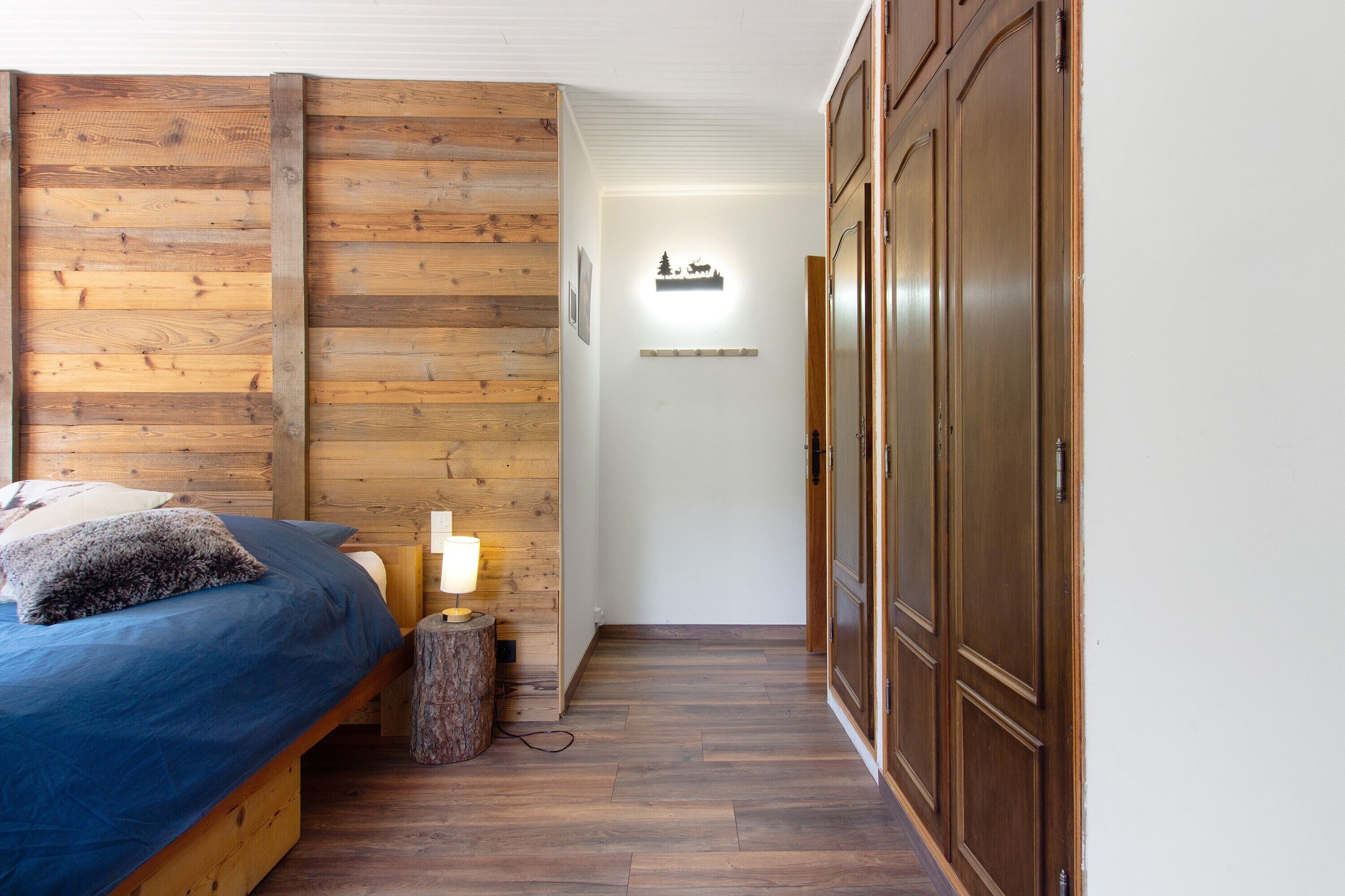 Une chambre à coucher avec une tête de lit en bois, un lit avec une literie bleue, une lampe de chevet et une armoire.