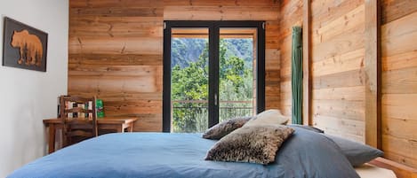 A bedroom with a large bed, a wooden wall, a window with a view of trees, and a bookshelf.