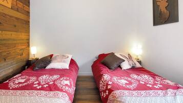 Een kamer met twee bedden, elk voorzien van een rode sprei en decoratieve kussens, een houten wand, en een decoratie van een hertenhoofd aan de muur.