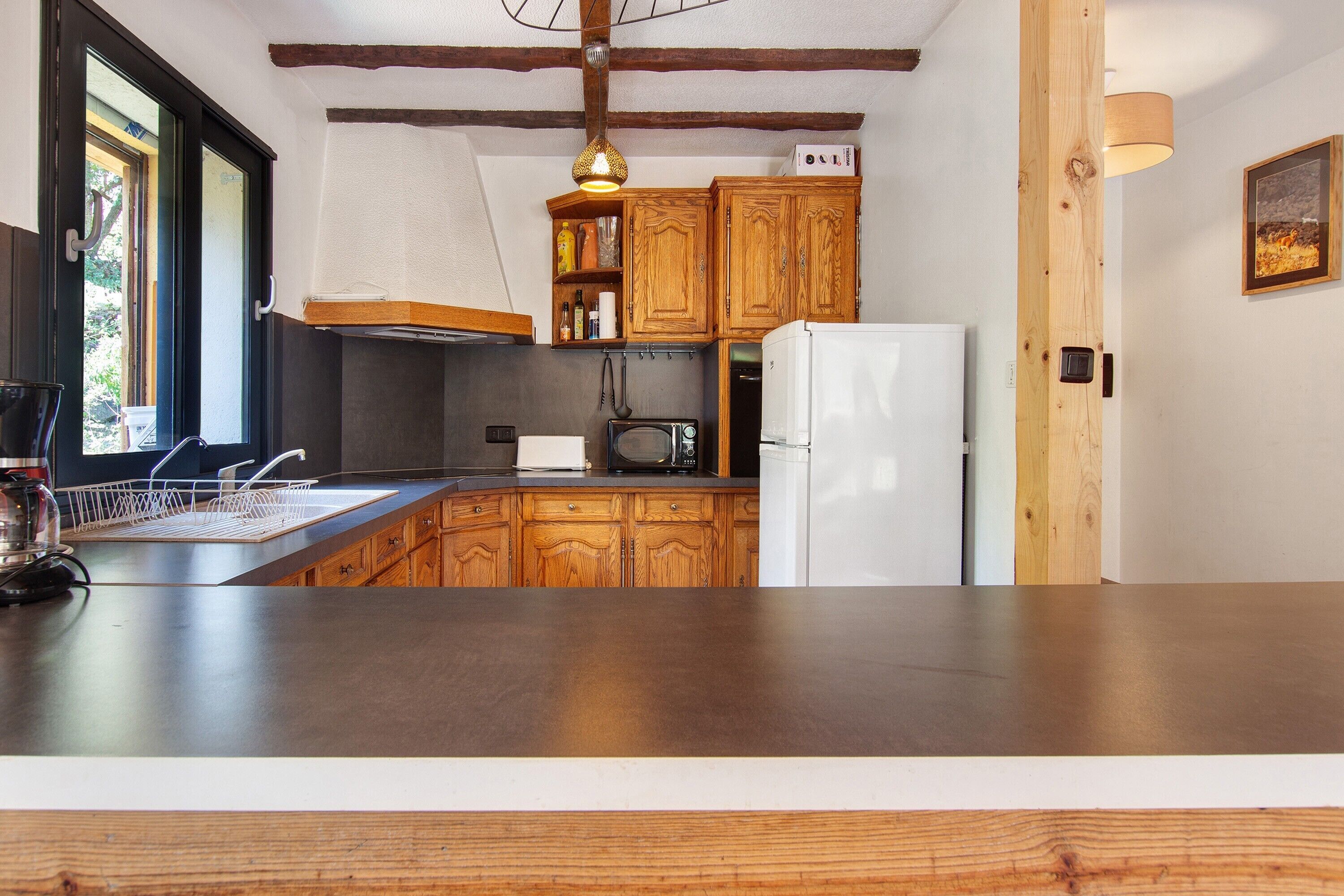 Une cuisine avec des meubles de rangement en bois, un réfrigérateur blanc, un four à micro-ondes et un luminaire suspendu.