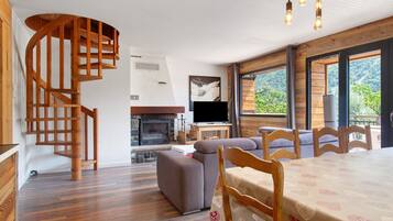 Een modern interieur met een houten trap, een open haard, een eethoek en grote ramen met uitzicht op de omgeving.