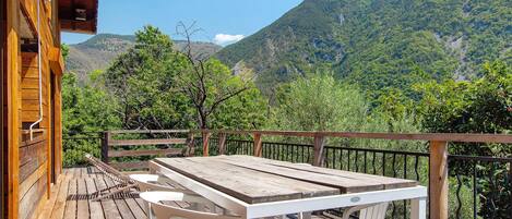 A wooden deck with a table and chairs, overlooking a mountainous landscape.