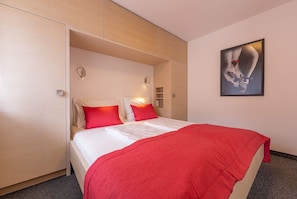 Una habitación de hotel con una cama, una manta roja y una obra de arte colgada en la pared.