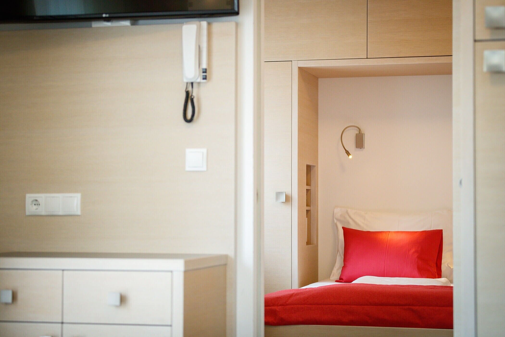 A hotel room with a bed, a bedside table, a wall-mounted phone, and a light switch.