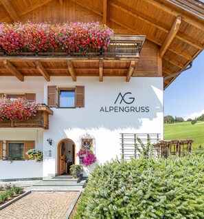 A building with a wooden balcony, a sign reading 'ALPENGRUSS,' and a stone pathway leading to the entrance.