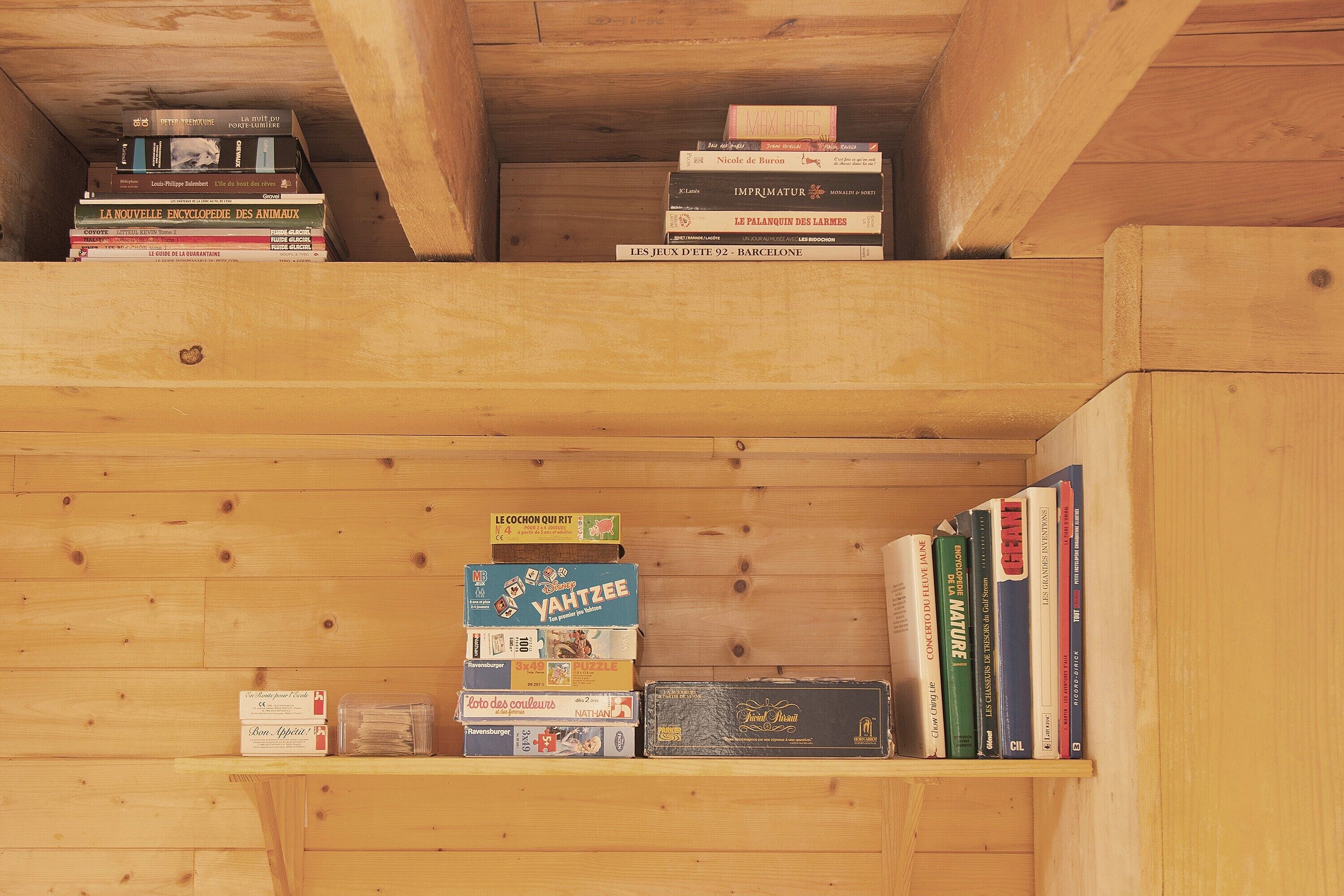 Une bibliothèque en bois contenant divers livres et jeux.