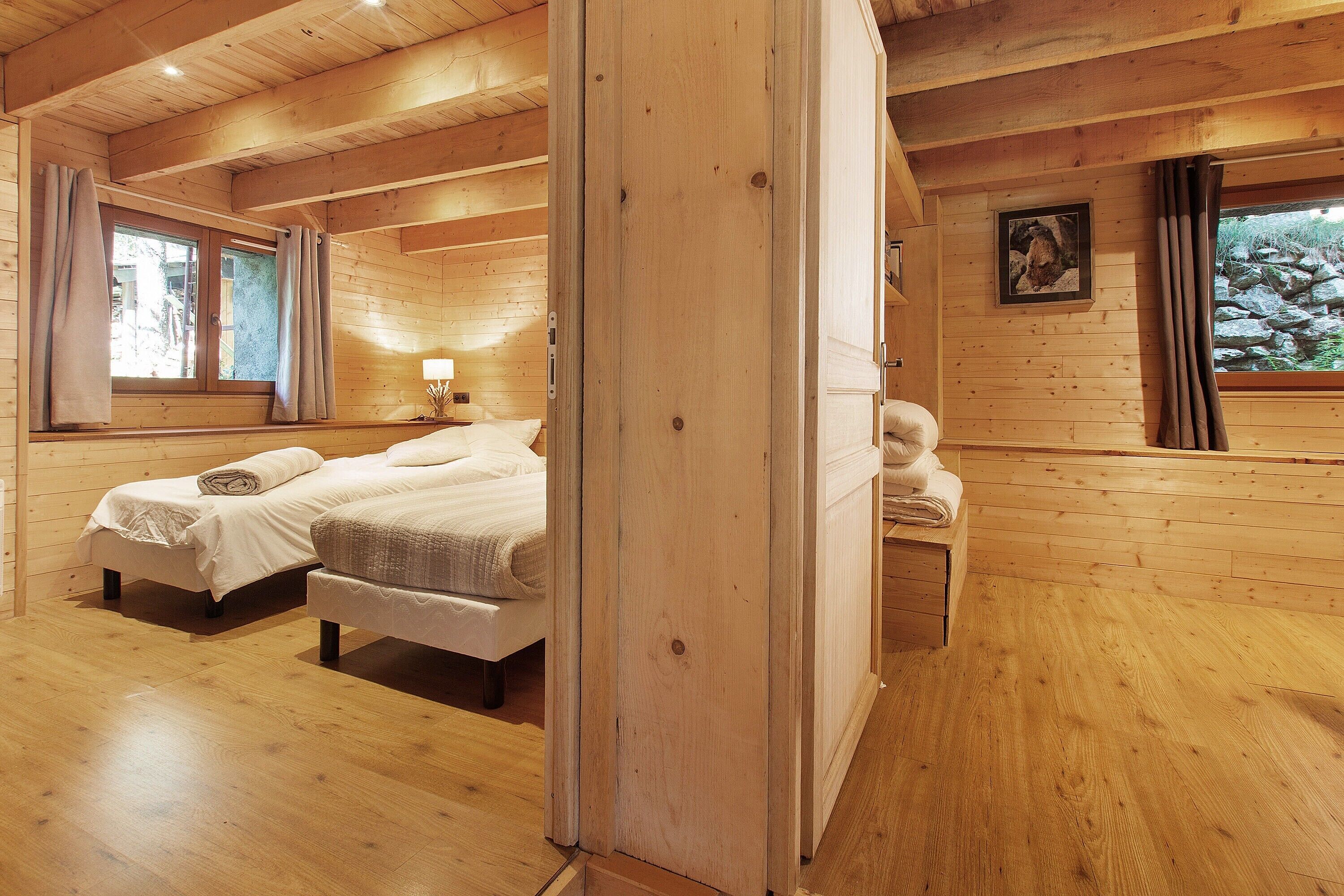 Een slaapkamer in een houten hutje met twee bedden, een nachtkastje, een lamp en een lijst met een foto aan de muur.