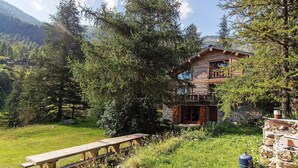 Een rustieke chalet met een stenen fundering, houten gevel en een balkon met uitzicht op een bebost gebied.