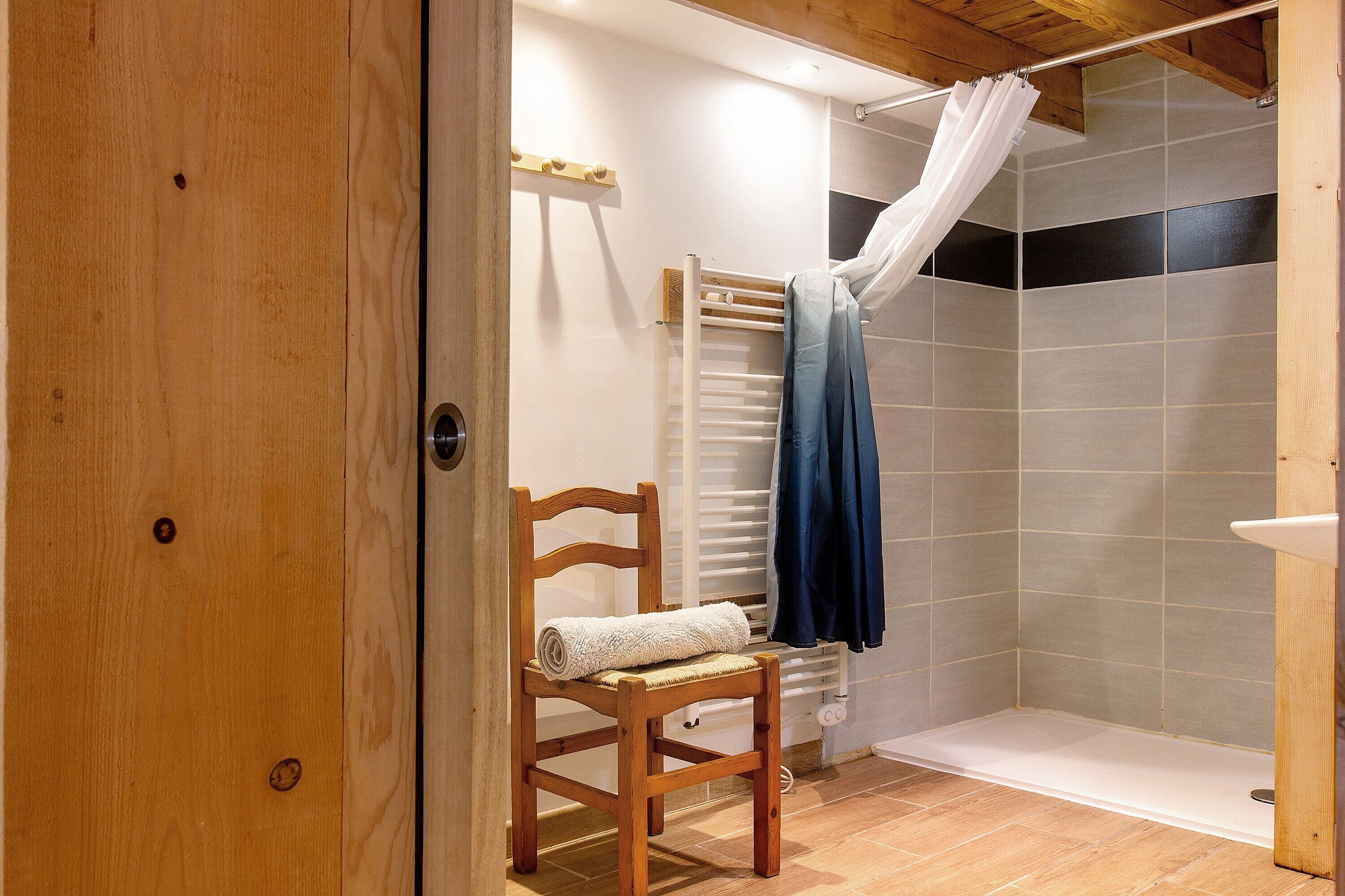 A wooden door leading to a bathroom with a shower, a towel on a chair, and a curtain.