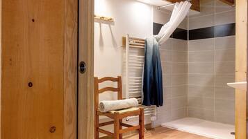 A wooden door leading to a bathroom with a shower, a towel on a chair, and a curtain.