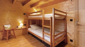 Een slaapkamer met een houten stapelbed, nachtkastje en lamp.