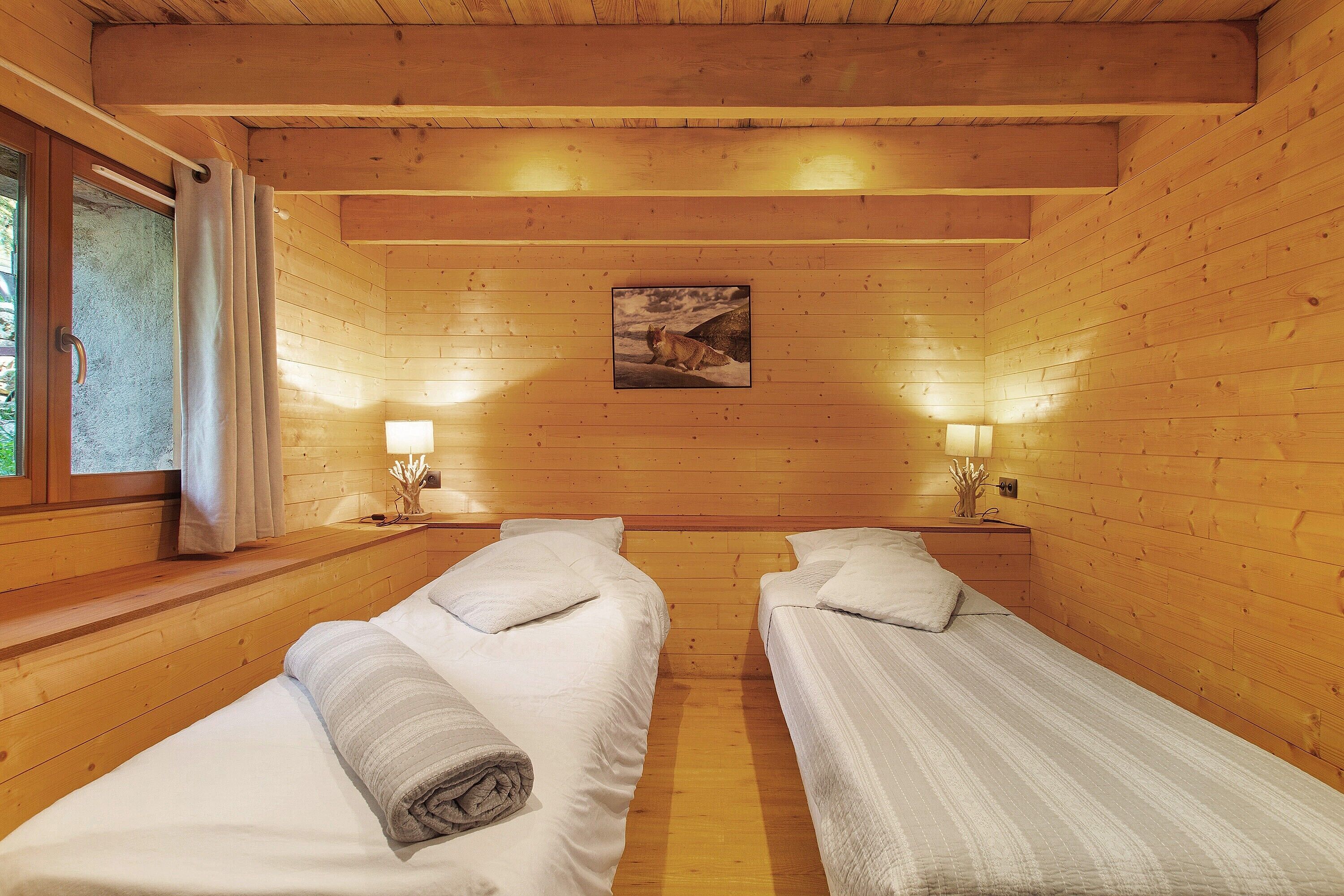 Une chambre rustique en bois avec deux lits, une fenêtre avec des rideaux et un tableau accroché au mur.