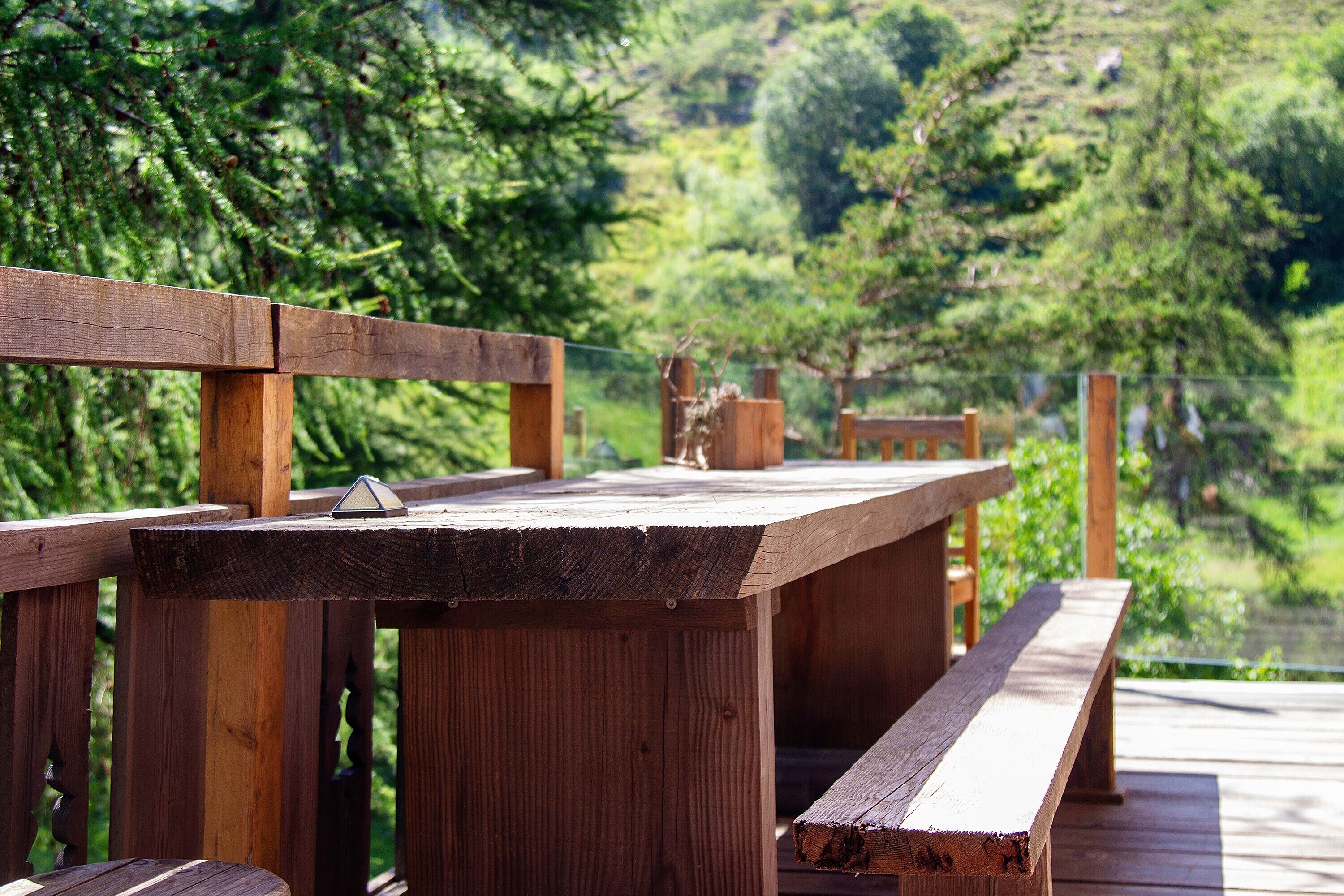 A wooden deck with benches and a table, surrounded by lush greenery.