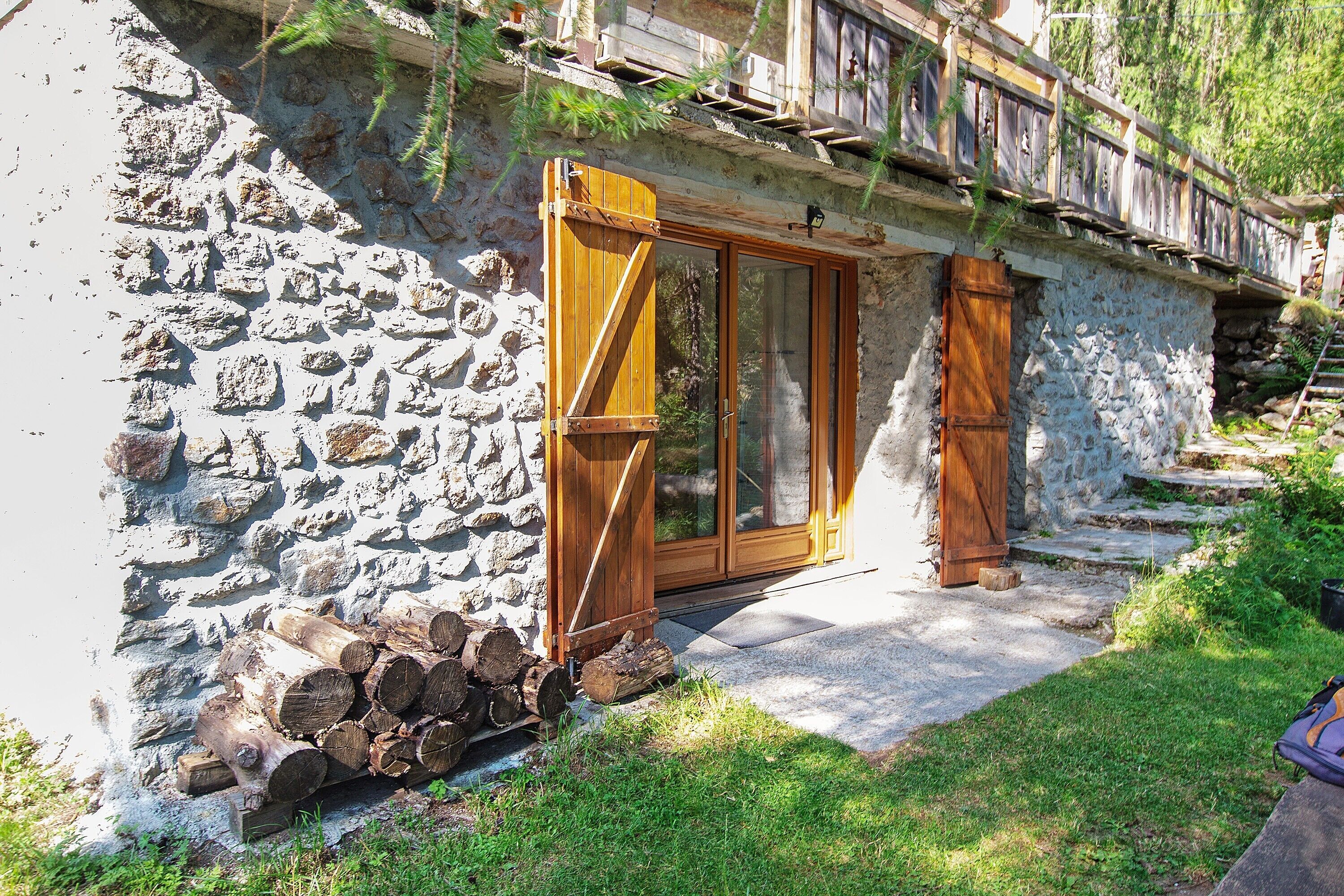 Un bâtiment en pierre avec une porte en bois et un escalier menant à une terrasse en bois.