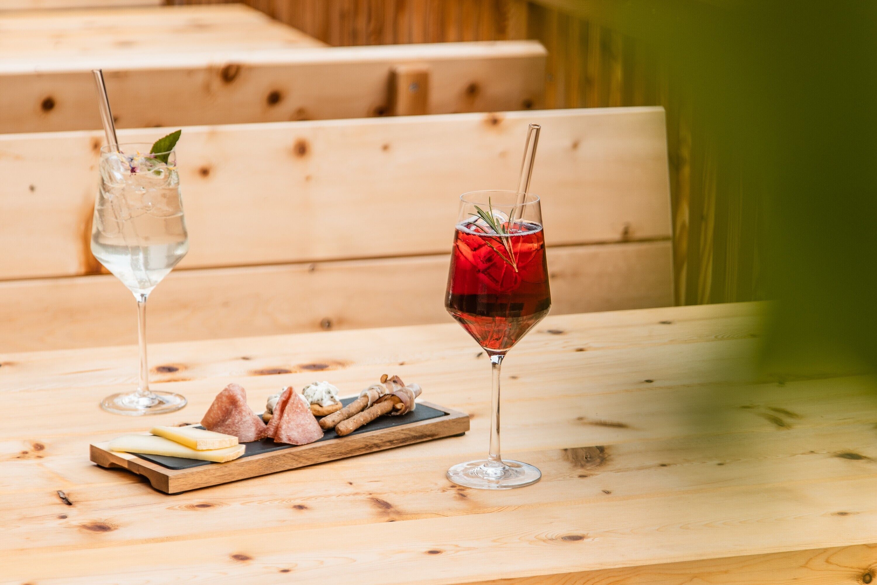 A wooden table with two glasses of beverages and a board of food items.