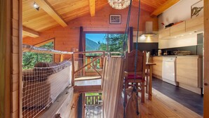 Interior de una cabaña de madera con cocina, comedor y balcón con vistas al exterior.