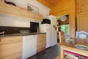 A compact kitchen with wooden cabinets, a dishwasher, a microwave, and a dining area with a table set for two. - Holiday Apartment "Gte T3 Le Balarino - Mercantour1" with Mountain View, Shared Garden & Wi-Fi (Belvédère)